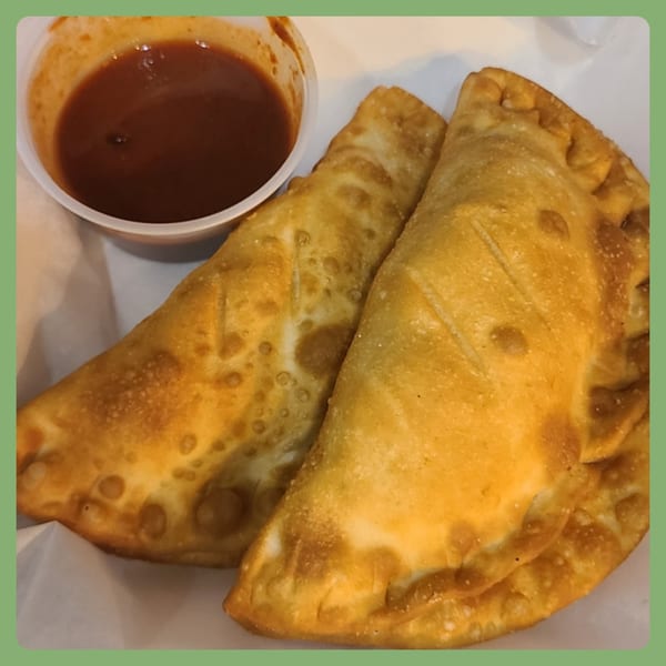 Two golden-brown empanadas with a side of red dipping sauce from Santa Fe Taco Company.