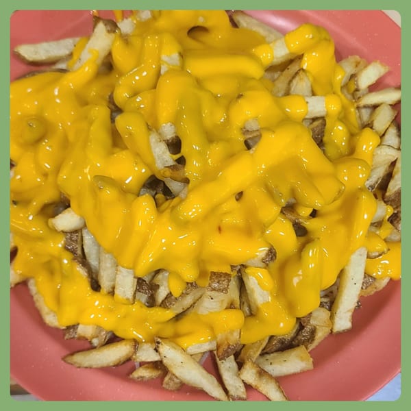 Close-up of golden french fries generously covered with bright yellow melted cheese sauce in a pink bowl.