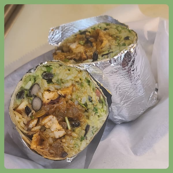 Two halves of a Santa Fe Taco Company burrito, filled with chicken, rice, black beans, and guacamole.