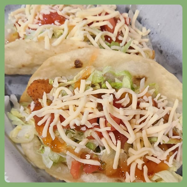 Two Santa Fe Taco Company tacos filled with meat, lettuce, tomatoes, cheese, and sauce.