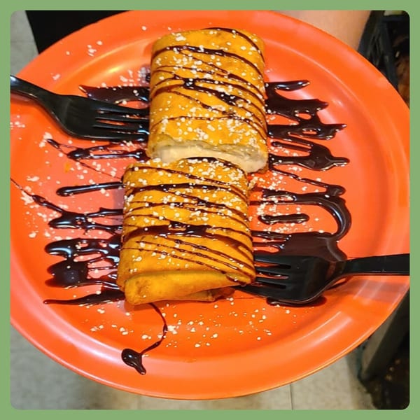 Two golden-fried dessert chimichangas drizzled with chocolate and powdered sugar on an orange plate.